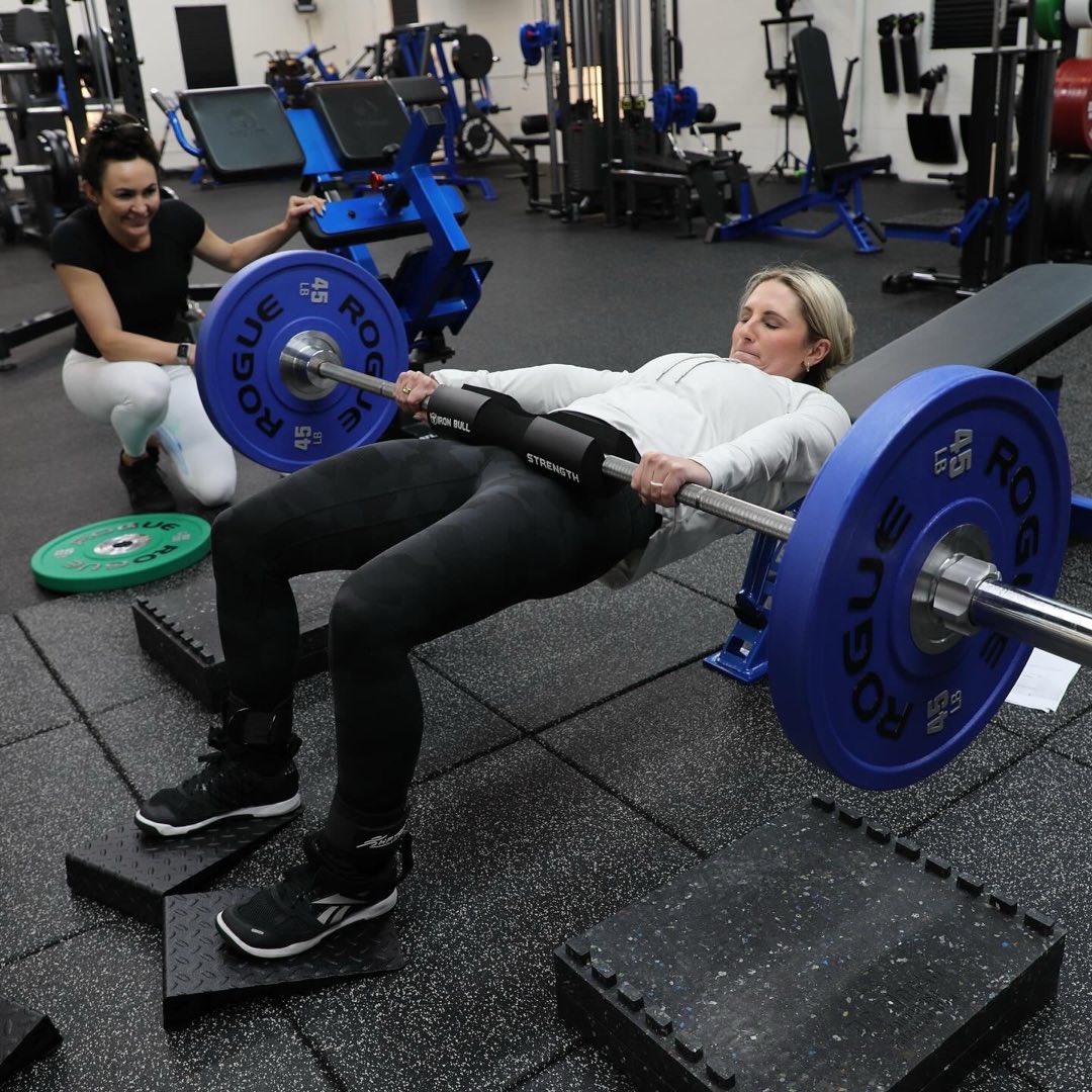 Val coaching a client through a barbell hip thrust in the gym