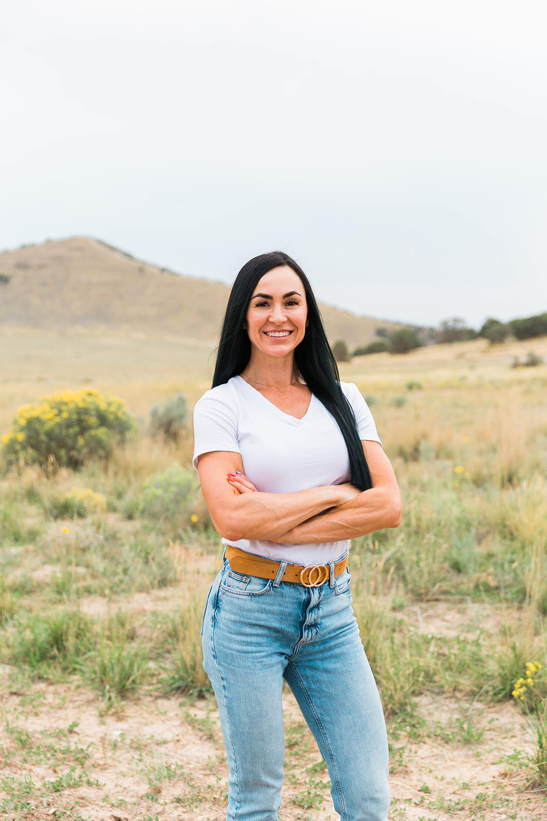 Val standing with arms folded in an open field